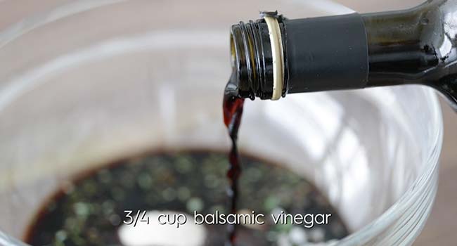 pouring balsamic vinegar into a bowl with herbs