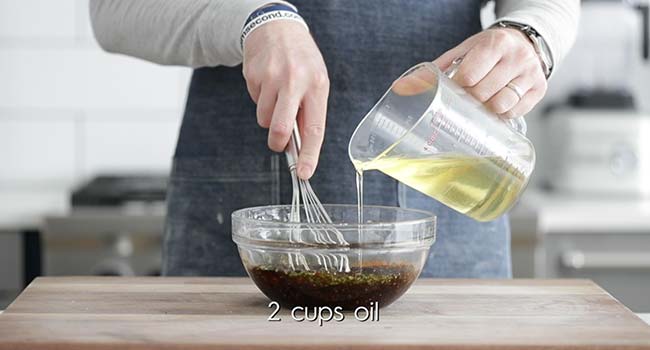 slowly pouring in oil to a bowl with vinegar while whisking