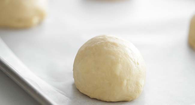 a rolled ball of brioche dough on a sheet tray with parchment paper