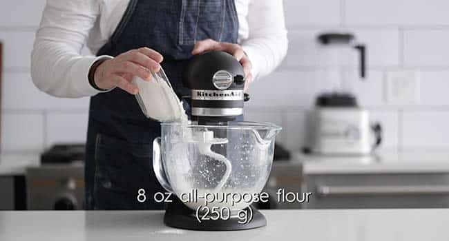 adding flour to a stand mixer with milk and yeast