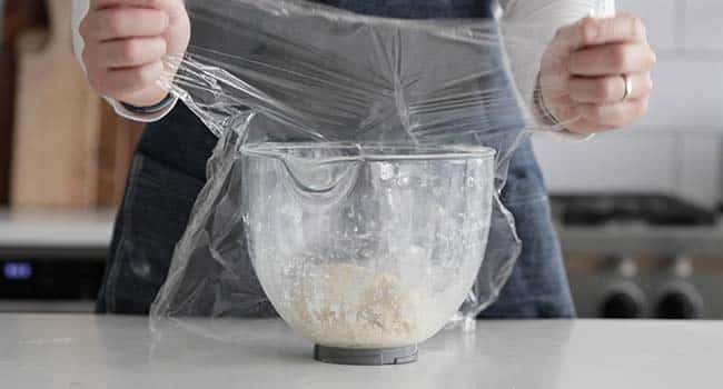 covering dough in a bowl with plastic wrap
