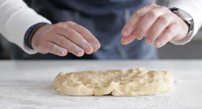 pressing dough out on a table to form a rectangle