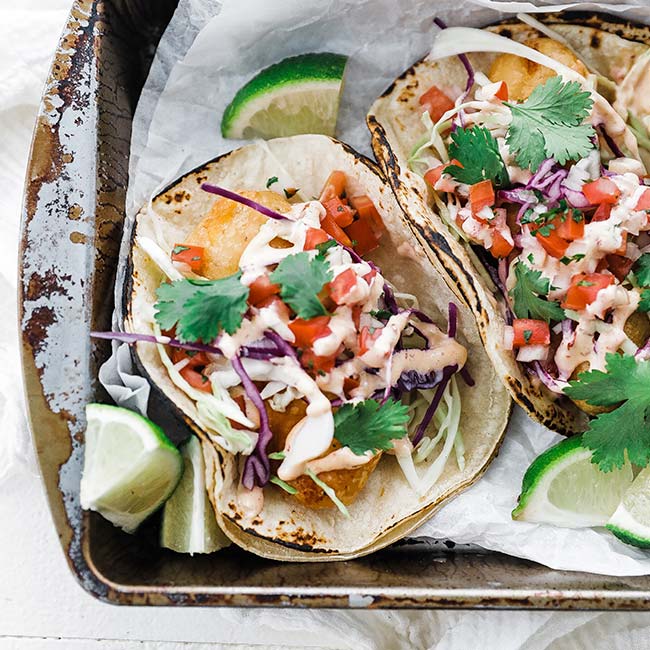 fish tacos on parchment paper with salsa and chipotle mayo