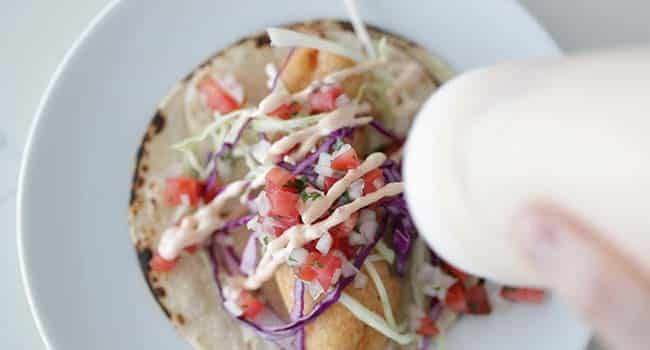 adding chipotle mayonnaise to a fish taco with salsa and cabbage