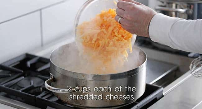 adding shredded cheese to a large pot with milk