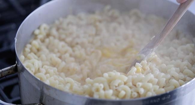 mixing together eggs, cheese sauce and cooked macaroni noodles together in a pot