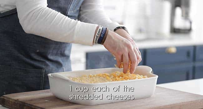 sprinkling cheese on top of macaroni and cheese in a casserole dish