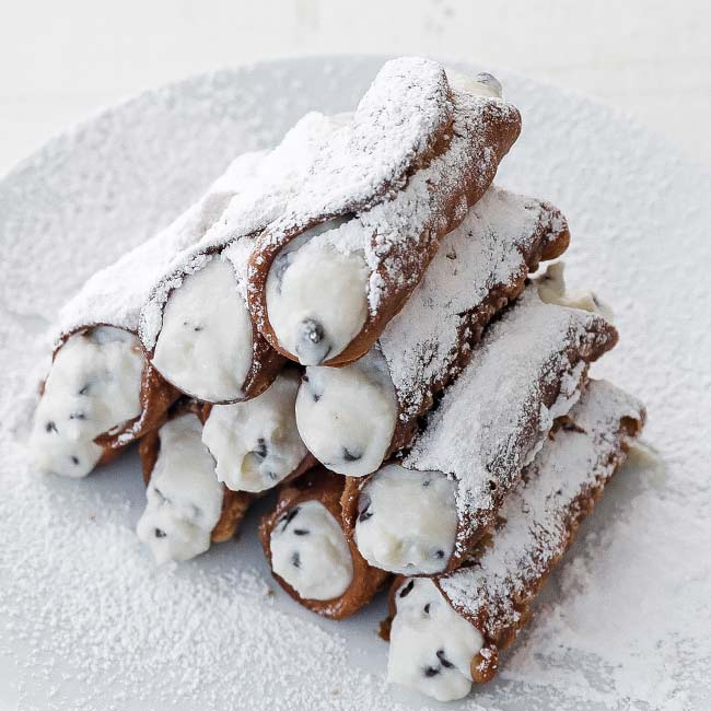 stacked up cannolis on a plate with powdered sugar