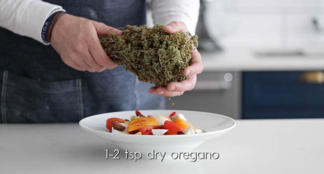 adding dry oregano onto tomatoes and cheese in a bowl