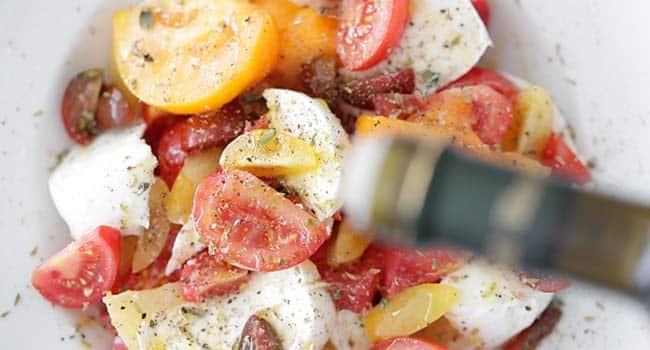 drizzling olive oil over tomatoes and cheese