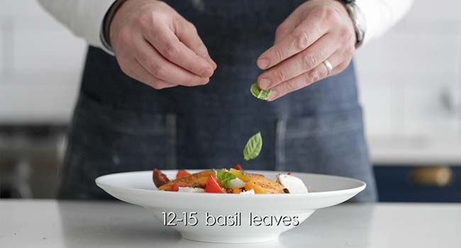 adding fresh basil leaves to tomatoes in a bowl