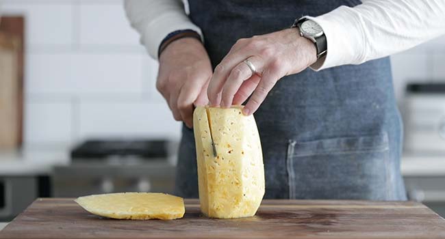 slicing a peeled pineapple on a cutting board