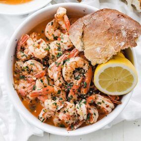 bowl of shrimp scampi with bread and lemon