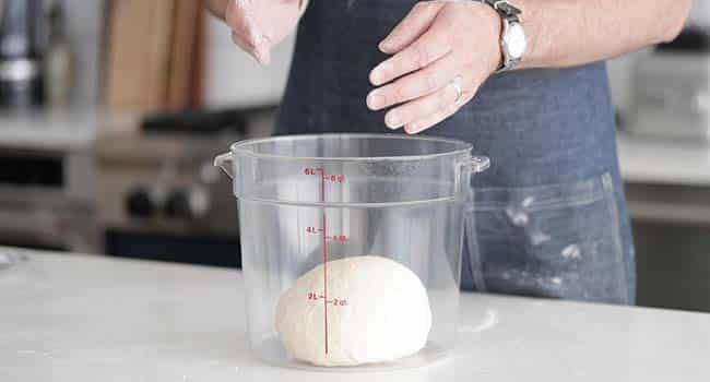 adding kneaded dough to a plastic container for proofing