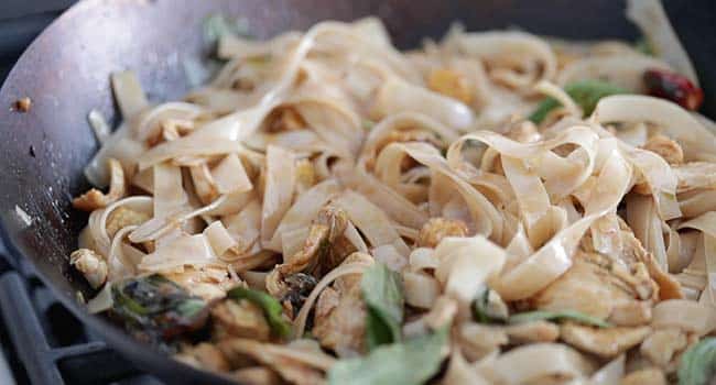 wide rice noodles coated in sauce with vegetables and basil