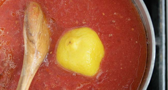 adding lemons to tomato sauce in a pot