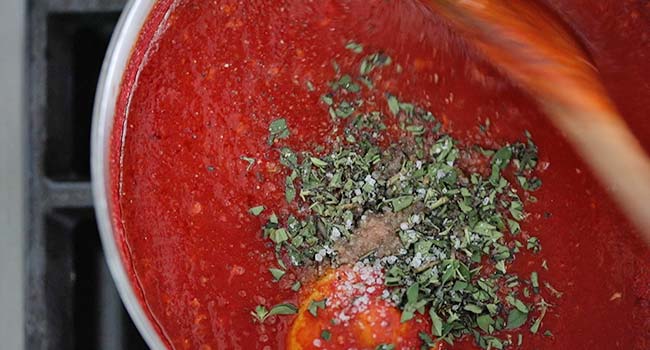 stirring in fresh oregano to tomato sauce