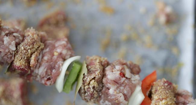 adding the breaded steak to a skewer with vegetables