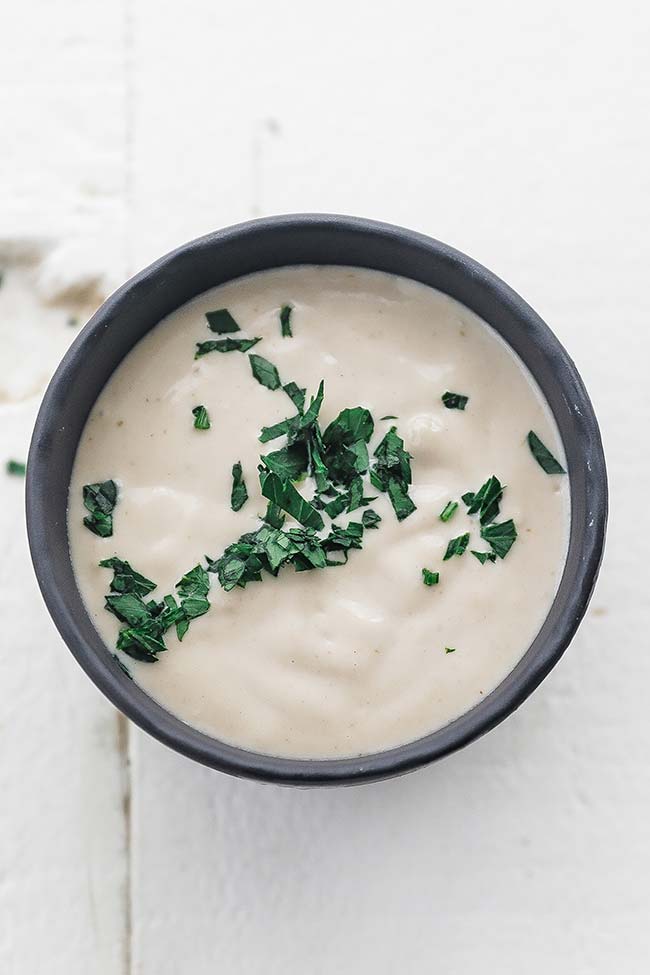 garlic tahini sauce in a bowl with chopped parsley