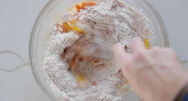 mixing eggs in a bowl with pumpkin and flour