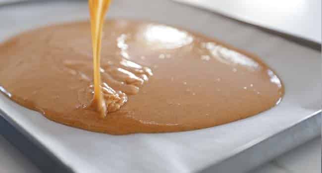 adding pumpkin batter to a sheet tray with parchment paper