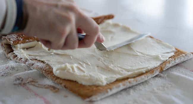 spreading cream cheese on a pumpkin cake