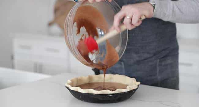 pouring a chocolate batter into a pie shell