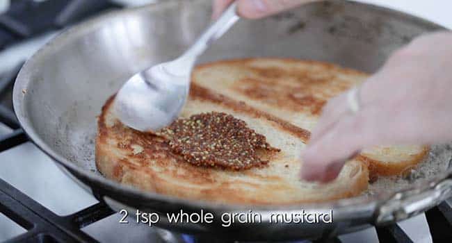 spreading whole-grain mustard on toasted bread in a pan