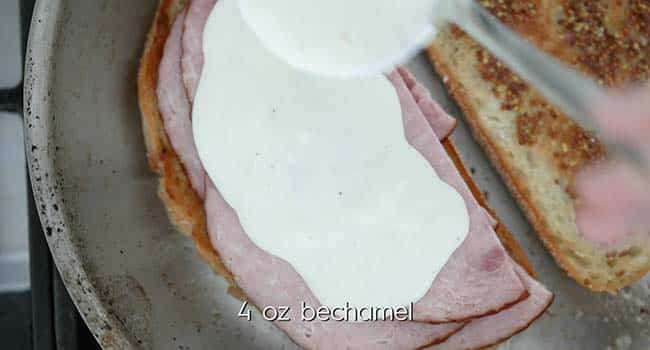 placing ham slices and bechamel sauce onto toasted piece of bread