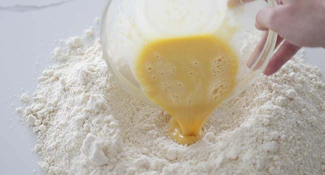 adding whisked eggs to the center of a flour well