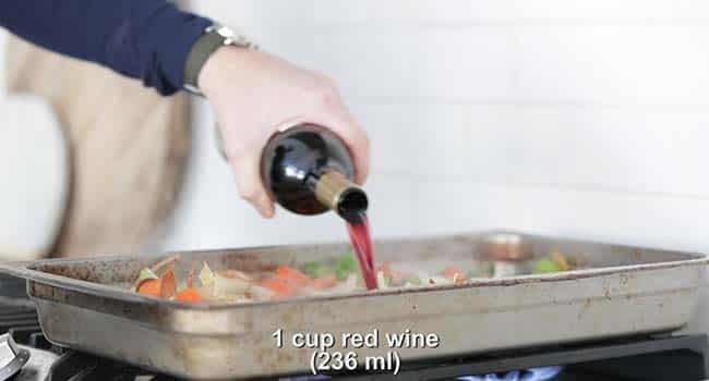 adding red wine to a pan with roasted vegetables