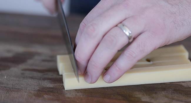 slicing chunks of swiss cheese on a cutting board