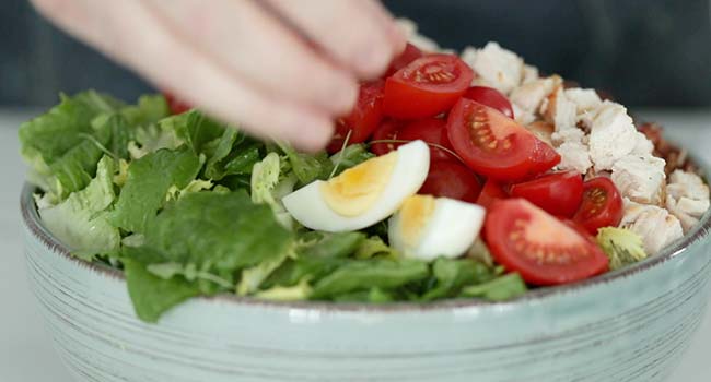 adding tomatoes and eggs to a salad