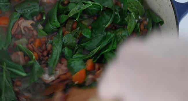 adding collards to a pot of cooked cowpeas