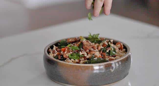 adding sliced green onions to a bowl of cooked hoppin' john