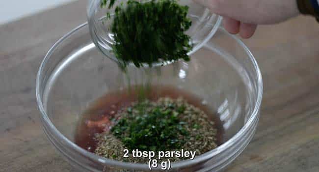 adding fresh herbs to a bowl with red wine vinegar