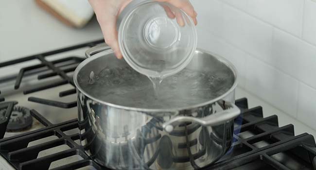 adding vinegar to a pot of boiling water