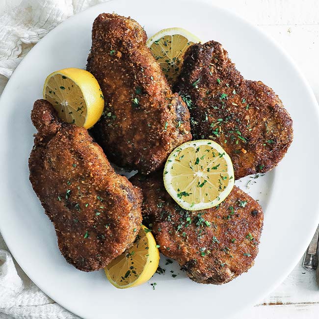 plate of cooked breaded pork chops with lemons