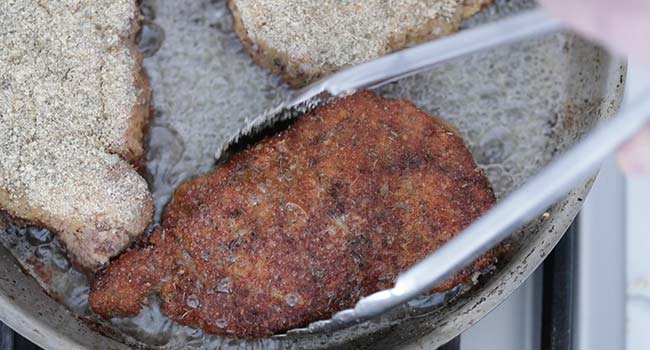 frying a breaded pork chop in a pan