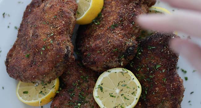 serving some breaded pork chops with lemons and parsley