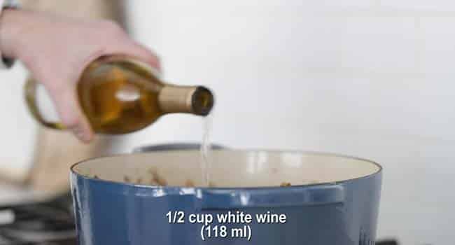 adding white wine to a large pot of mushrooms