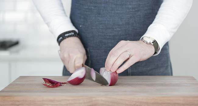 slicing a red onion in half on a cutting board