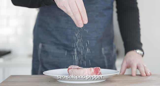 seasoning a steak on a plate with salt