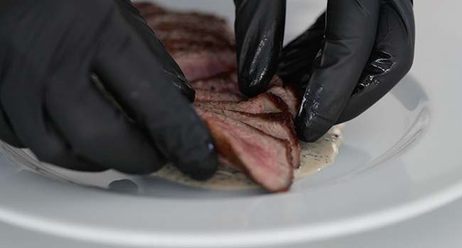 adding a steak au poivre to a plate with cream sauce