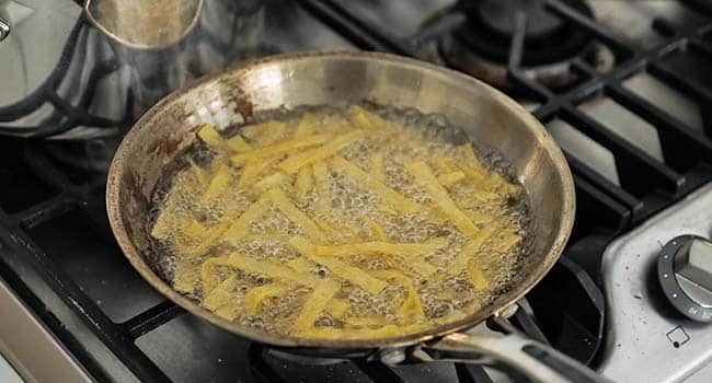 frying tortillas in oil in a pan