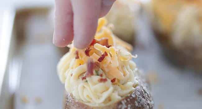 adding shredded cheese and bacon to a stuffed potato