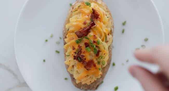 garnishing a cooked twice-baked potato with chopped chives