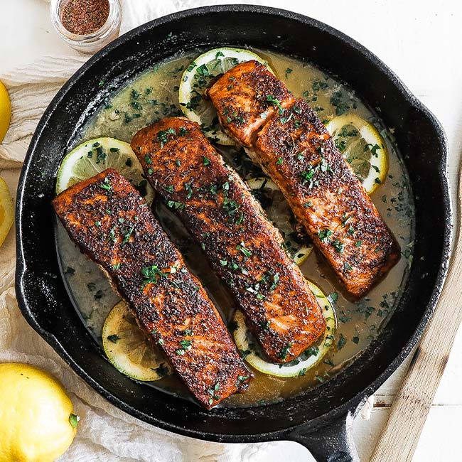 blackened salmon fillets in a cast iron skillet with lemons