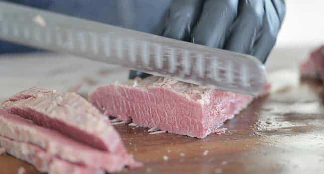 slicing cooked corned beef on a cutting board