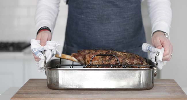 a roasted bone in leg of lamb in a roasting pan with a rack